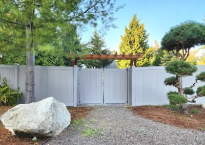 Gray vinyl privacy fence with double gate and wooden pergola installed in a landscaped backyard in Seattle