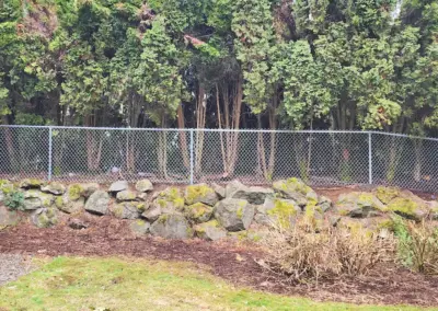 Chain link fence installed on stone retaining wall near wooded area